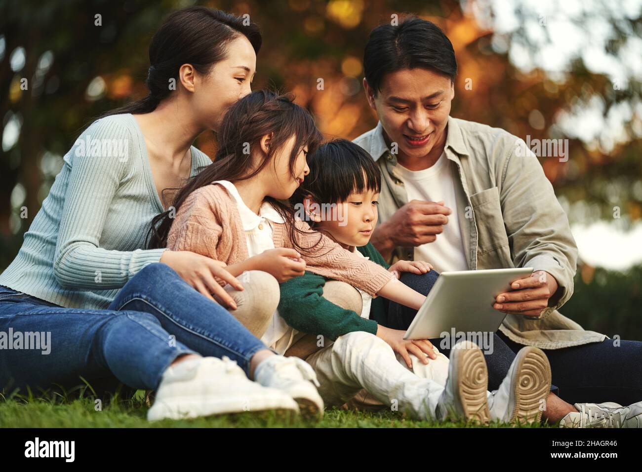 une famille asiatique heureuse avec deux enfants qui s'assoit sur l'herbe pour se détendre dans le parc de la ville au coucher du soleil Banque D'Images