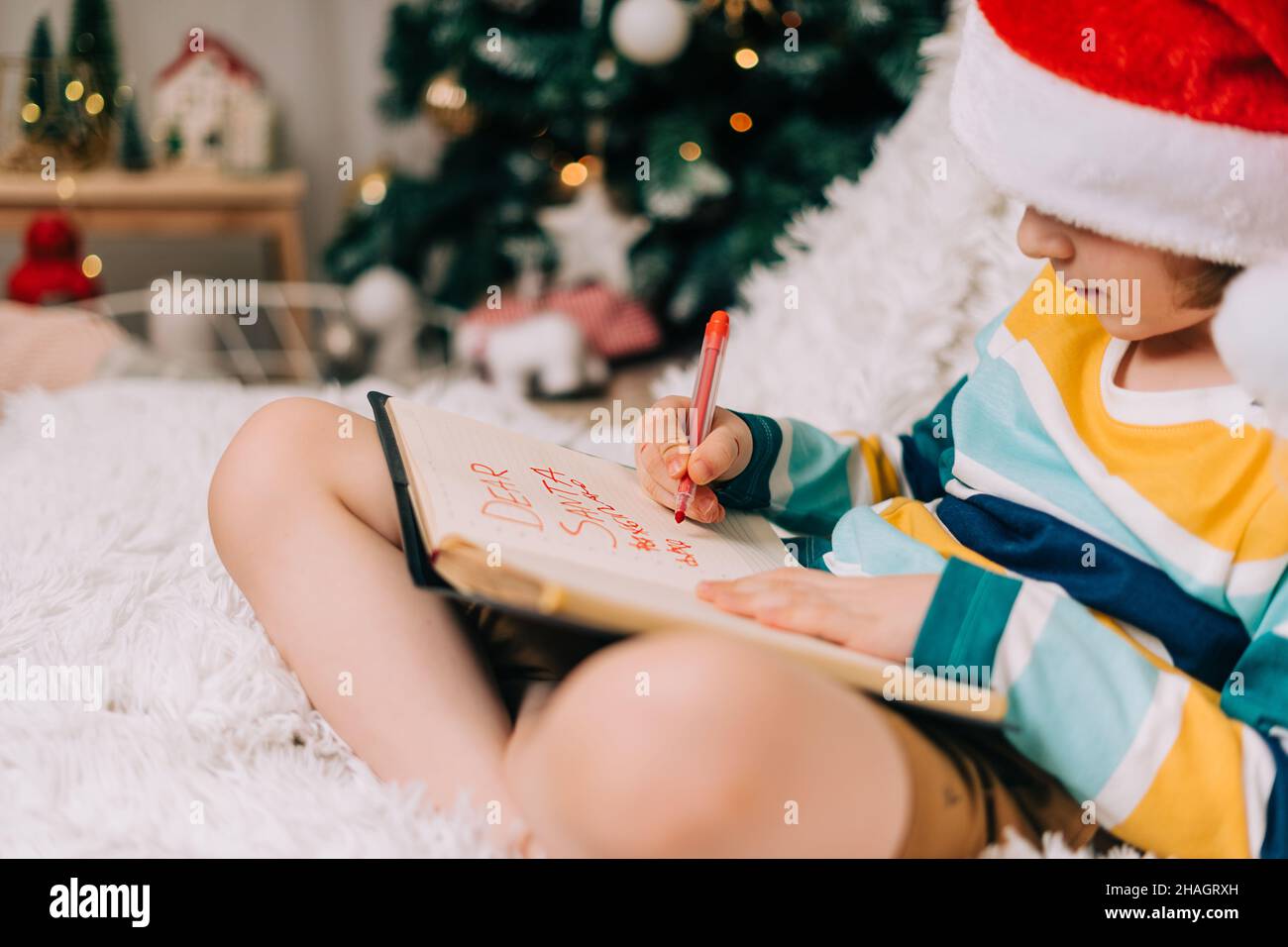 Enfant garçon dans le chapeau de père Noël rouge écrivant la lettre et le dessin à cher père Noël à la maison.Liste de souhaits enfant.Rêves de cadeaux de Noël.Joyeux Noël et heureux Banque D'Images