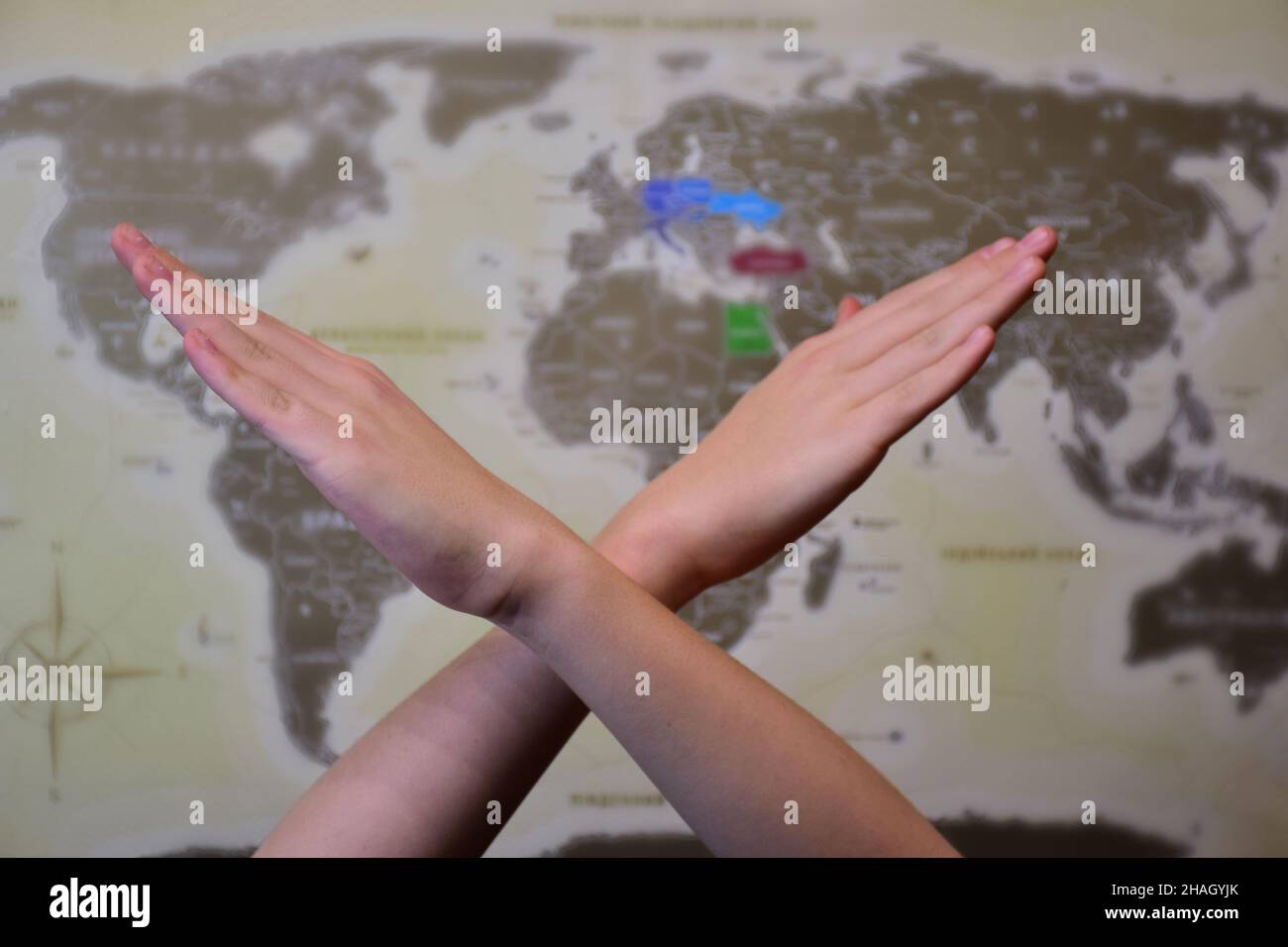 Deux mains humaines croisées dans un signe d'interdiction devant une carte du monde avec un arrière-plan très flou Banque D'Images