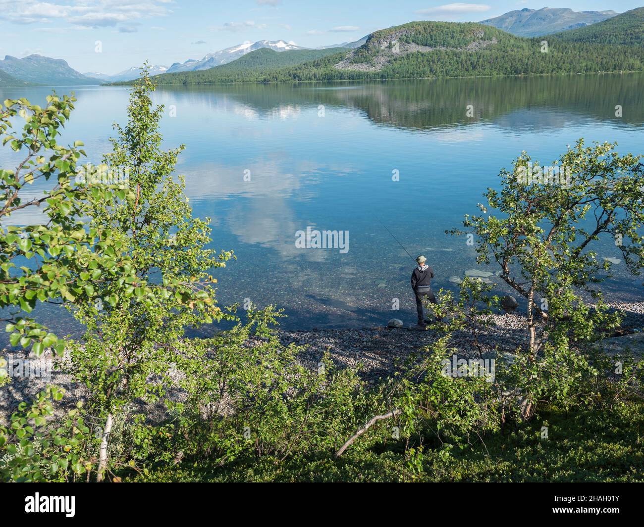 Pêcheur à la rivière Lule, dans un calme clair Lac de barrage de Lulealven eau douce à Saltoluokta en Suède Laponie à la belle journée d'été.Montagne rocheuse verte Banque D'Images