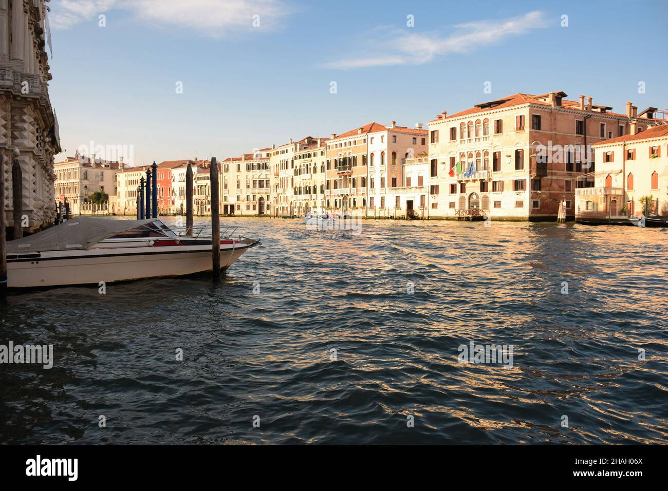 Un large canal dans la Venise italienne entre des bâtiments anciens, éclairés par le soleil, avec des bateaux dessus. Banque D'Images