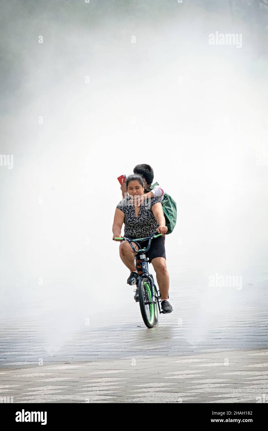 Une mère émerge de la Fontaine des Foires, un jardin de brume qui reproduit un de la Foire du monde 64.À Flushing Meadows Park, Queens, New York. Banque D'Images