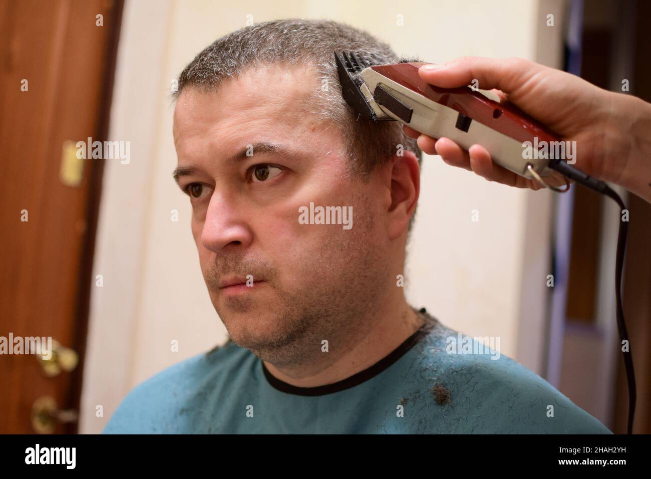 Un homme adulte est tondu avec une tondeuse à cheveux et s'assoit face à l'appareil photo.Peut-être à la maison dans un verrouillage Banque D'Images