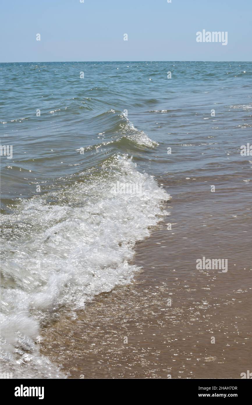 Des vagues de mer mousseuse roulent sur la plage de sable de jour Banque D'Images