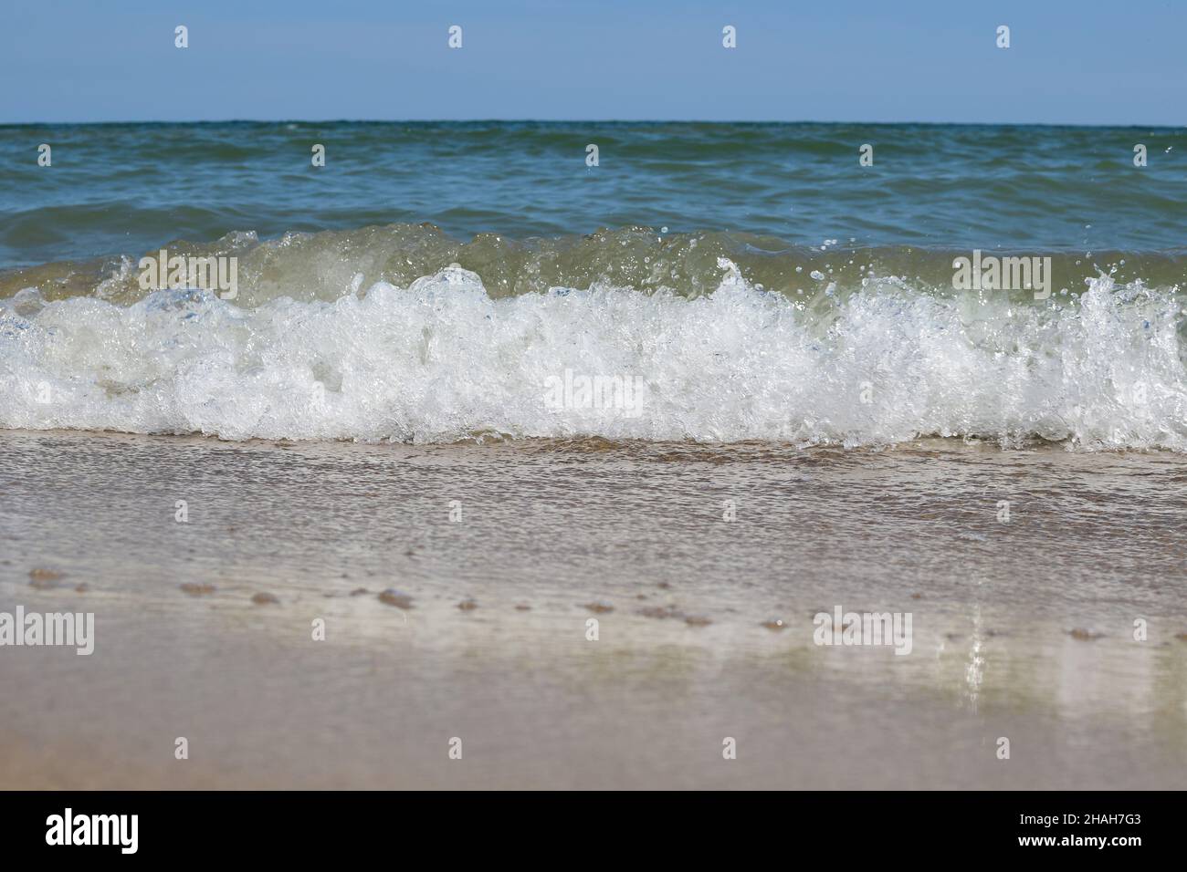 Des vagues de mer mousseuse roulent sur la plage de sable de jour Banque D'Images