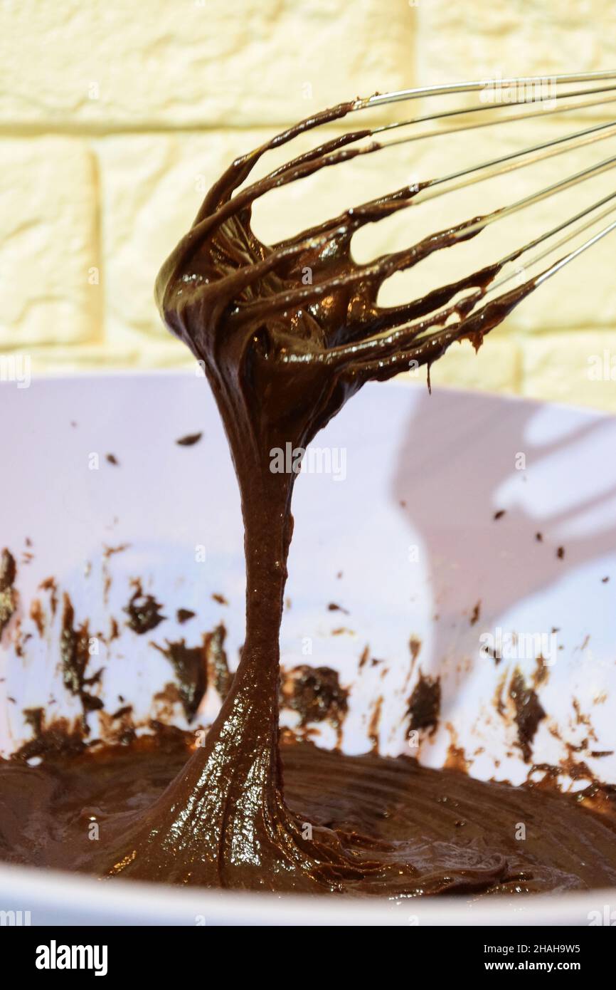 Faire du chocolat à la maison.Liquide et foncé sur un fond flou fouetté avec un fouet dans une plaque en plastique Banque D'Images