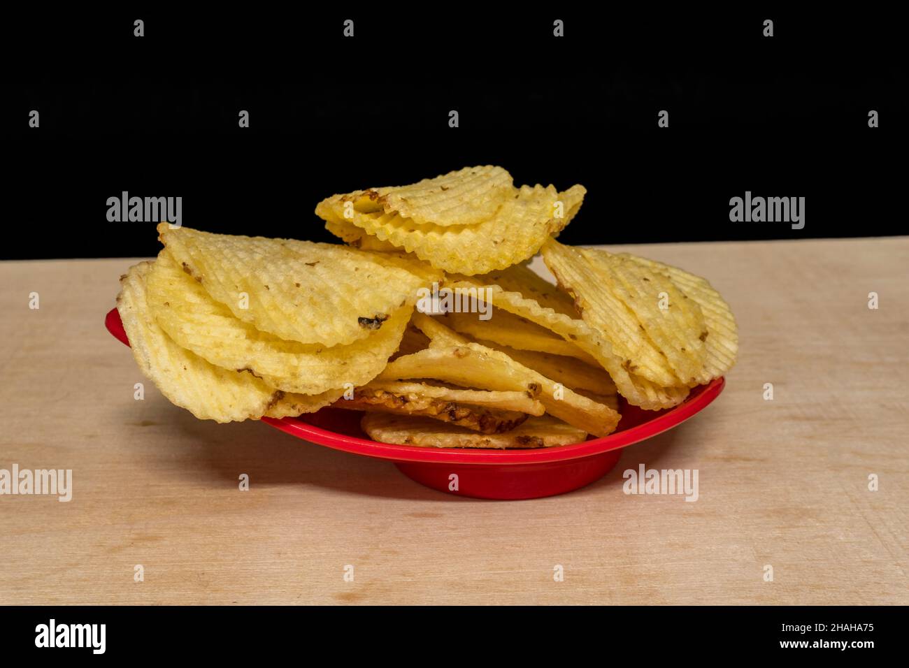 Gaufrettes de pommes de terre salées dans un bol rouge sur une table en bois, tas de gaufrettes, espace de copie, tas de frites, vue latérale Banque D'Images