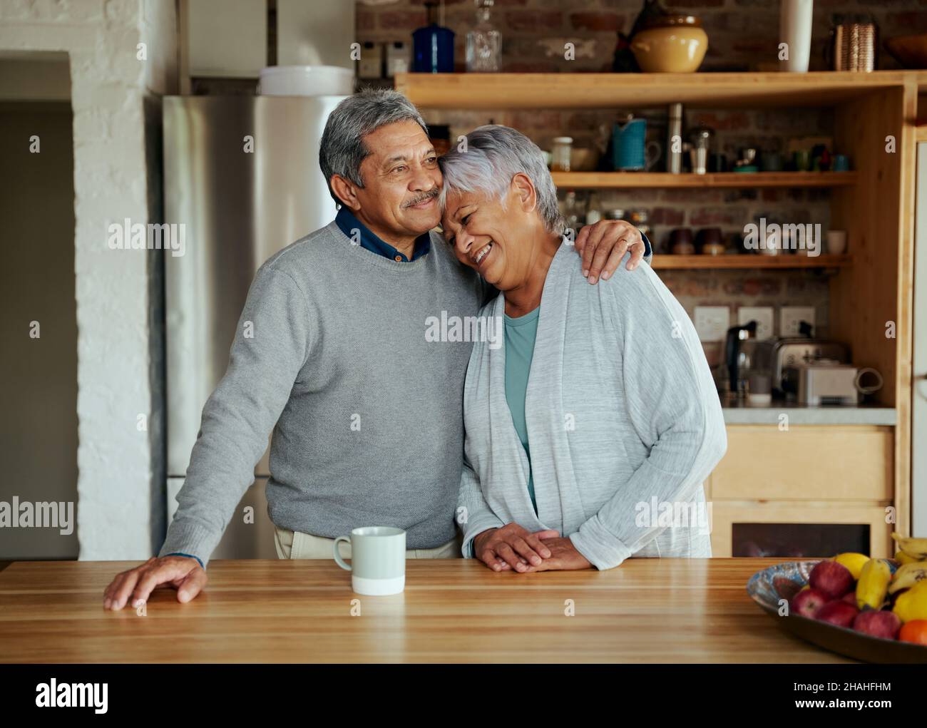 Heureusement, un couple biracial âgé à la retraite se tenant les uns les autres avec amour dans une cuisine moderne. Banque D'Images