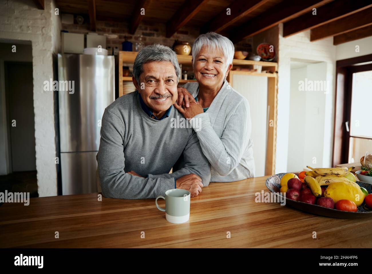 Portrait d'un couple biracial âgé à la retraite heureux, penché sur le comptoir de la cuisine, souriant à l'appareil photo.Un style de vie sain dans une cuisine moderne. Banque D'Images