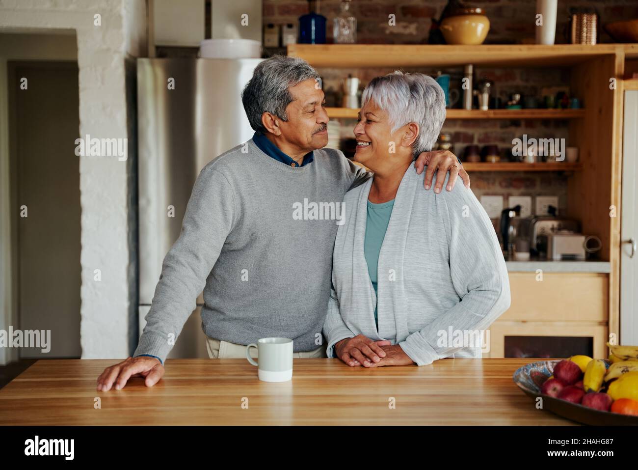 Heureusement, un couple biracial âgé à la retraite se souriant les uns les autres dans une cuisine moderne.Un style de vie sain et enviant dans une cuisine moderne. Banque D'Images