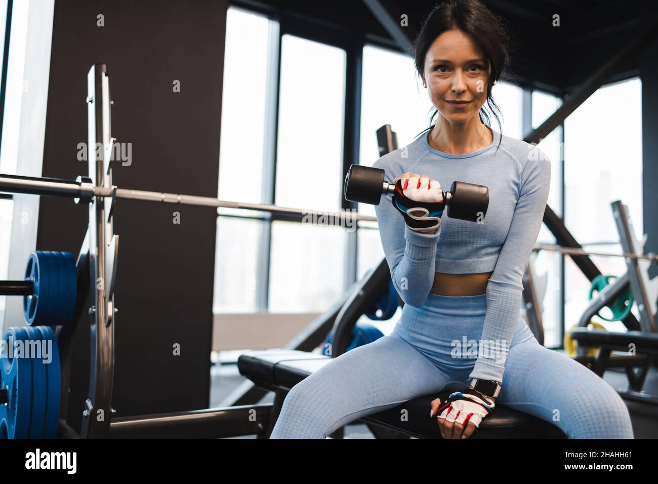 Une femme secoue des biceps levant une haltère tout en étant assise sur un banc dans la salle de gym Banque D'Images