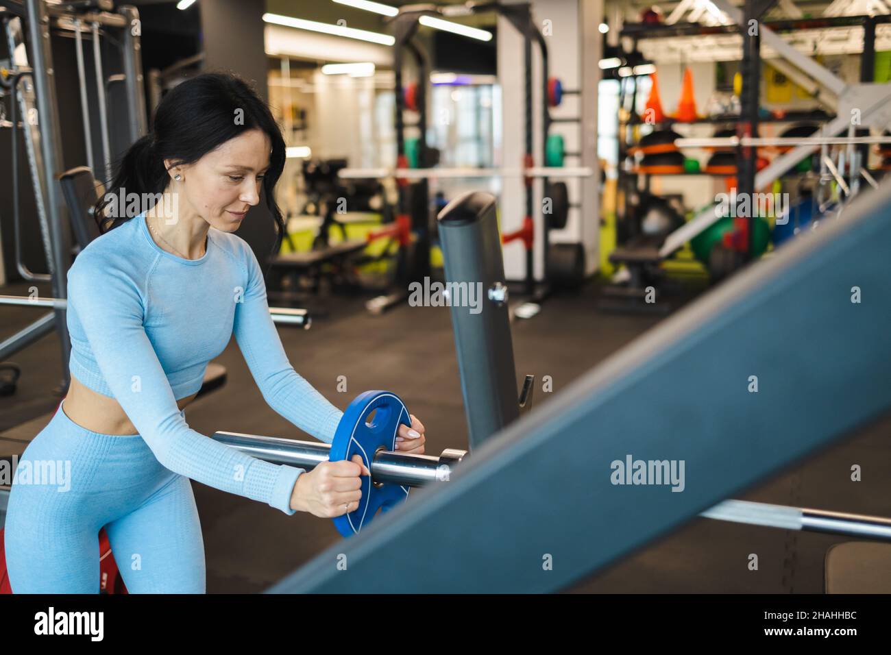Femme sportive mettant un disque de métal sur la barbell pendant l'entraînement Banque D'Images