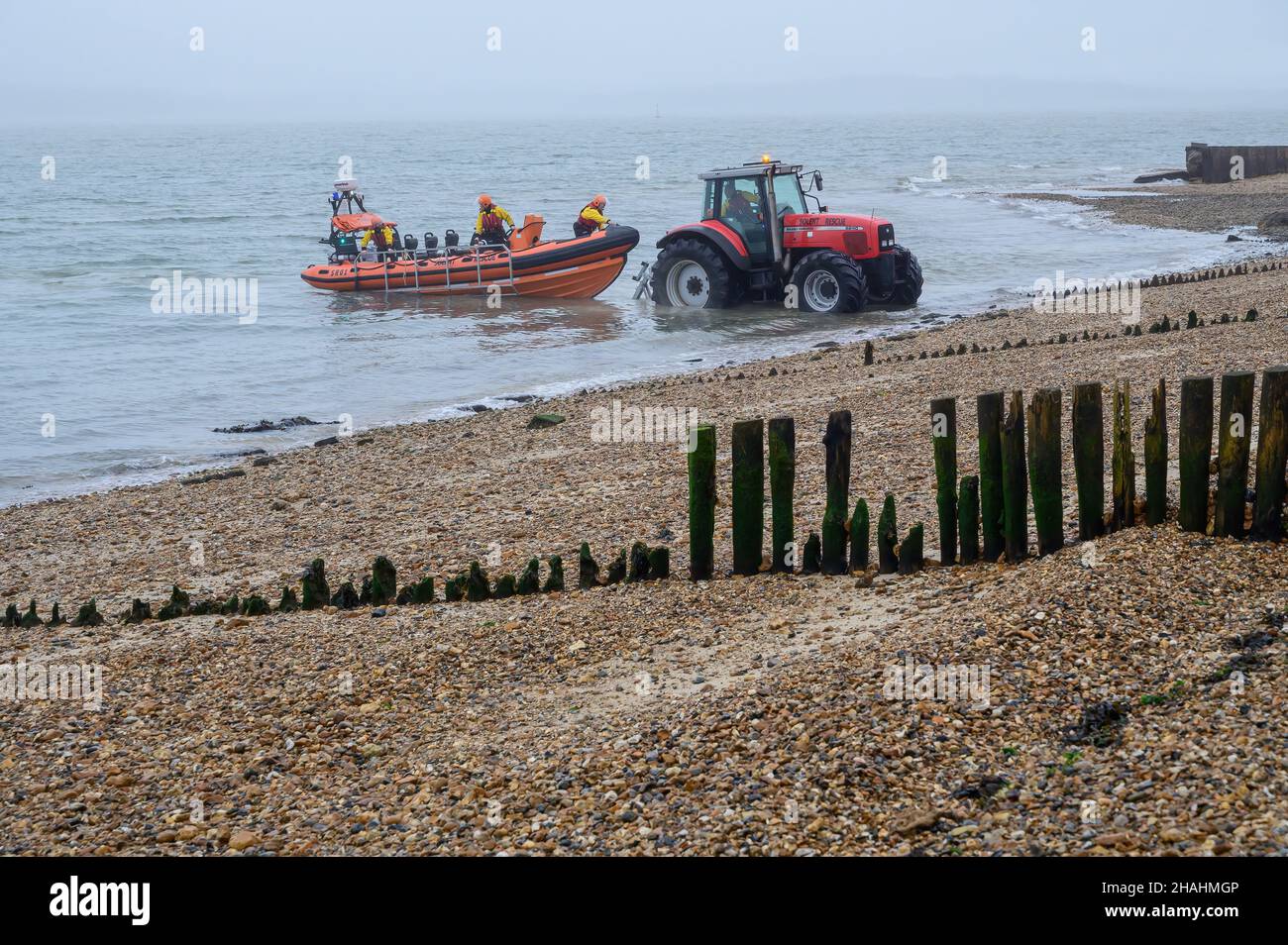 Tracteur rouge abaissant le bateau de sauvetage Solent dans la mer depuis la rive de galets et les groynes en bois lors d'une matinée brumeuse à la plage de Lepe.Lepe Country Park. Banque D'Images