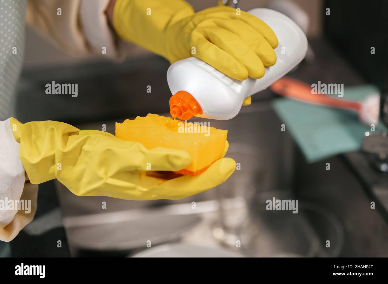 Gros plan des mains dans des gants jaunes versant du détergent sur une éponge Banque D'Images