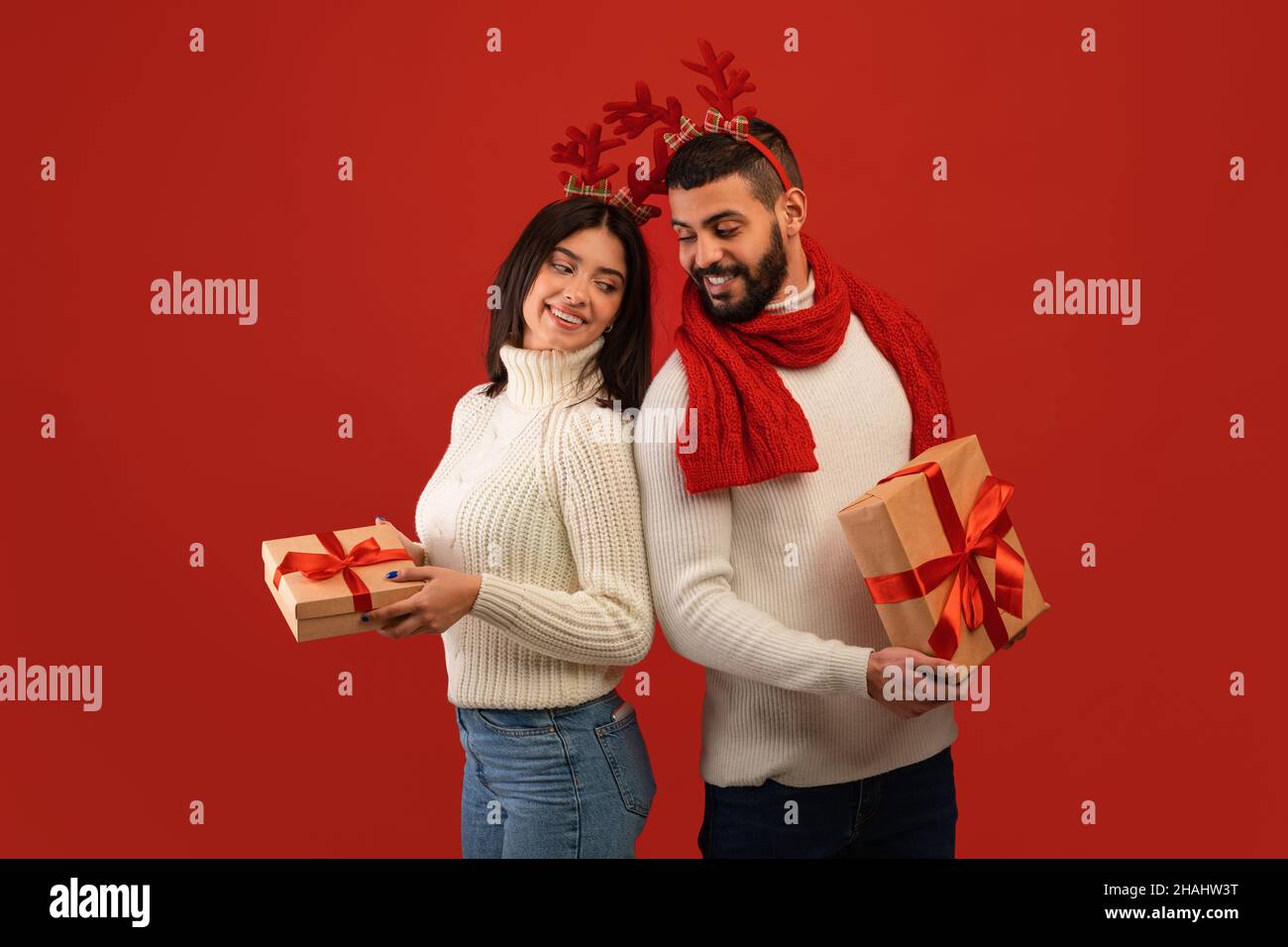 Jeune heureux Moyen-Orient couple dans les cornes de cerf tenant des boîtes cadeaux de Noël, prêt à échanger des cadeaux de Noël Banque D'Images