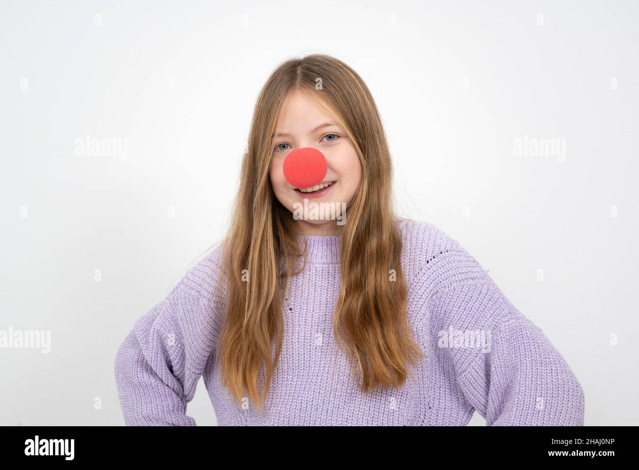 belle jeune fille avec le nez de clown rouge posant devant le fond blanc et porte un chandail en laine pourpre Banque D'Images