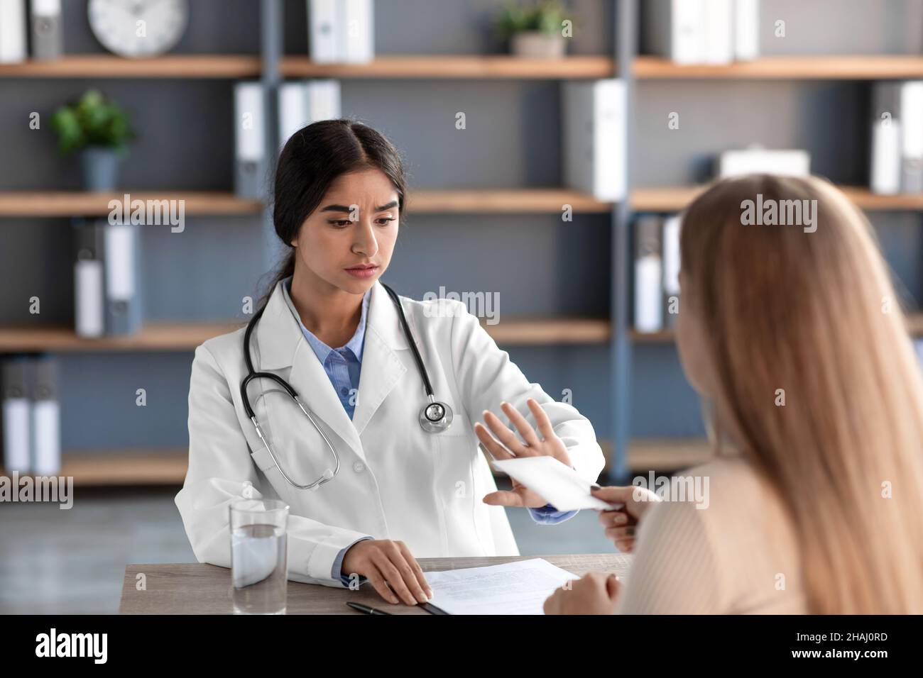 Choqué jeune femme indienne médecin en manteau blanc avec stéthoscope refuse de l'argent du patient Banque D'Images