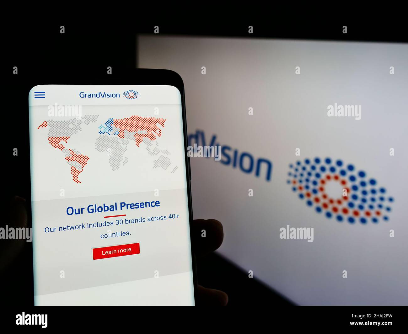Personne tenant un téléphone portable avec le site Web de la société hollandaise de vente au détail optique GrandVision N.V. à l'écran avec logo.Concentrez-vous sur le centre de l'écran du téléphone. Banque D'Images