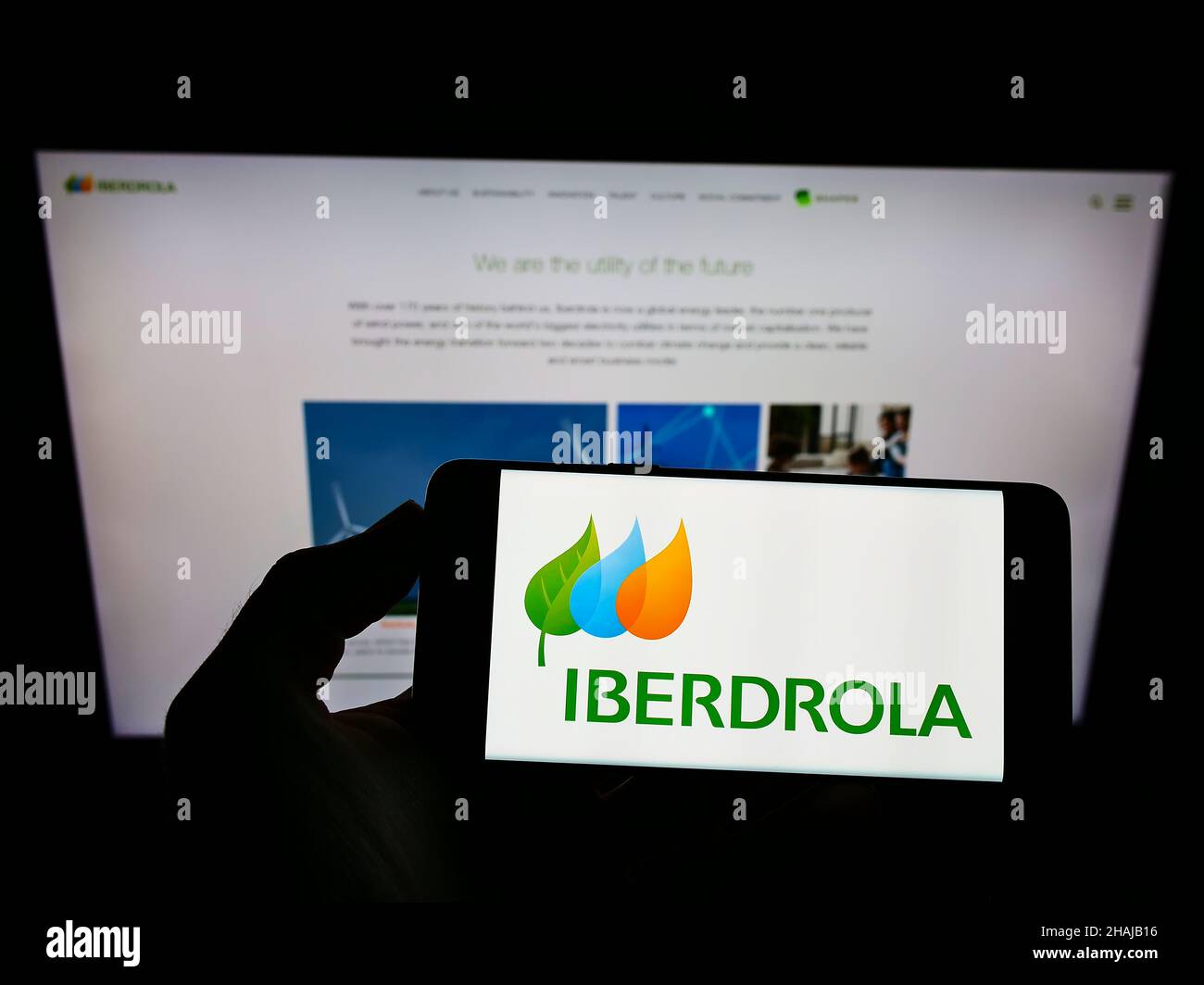 Personne tenant le téléphone portable avec le logo de la société espagnole d'électricité Iberdrola sa à l'écran en face de la page web d'affaires.Mise au point sur l'affichage du téléphone. Banque D'Images
