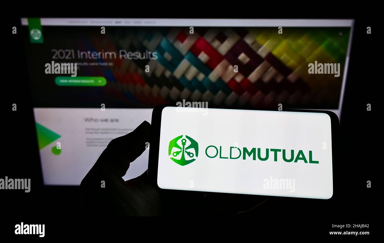 Personne tenant un smartphone avec le logo de la société financière africaine Old Mutual Limited (OML) sur l'écran devant le site Web.Mise au point sur l'affichage du téléphone. Banque D'Images