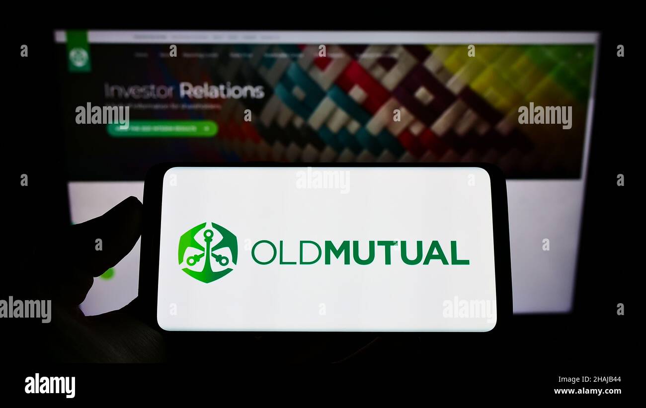 Personne tenant un téléphone portable avec le logo de la société financière africaine Old Mutual Limited (OML) sur l'écran en face de la page Web.Mise au point sur l'affichage du téléphone. Banque D'Images