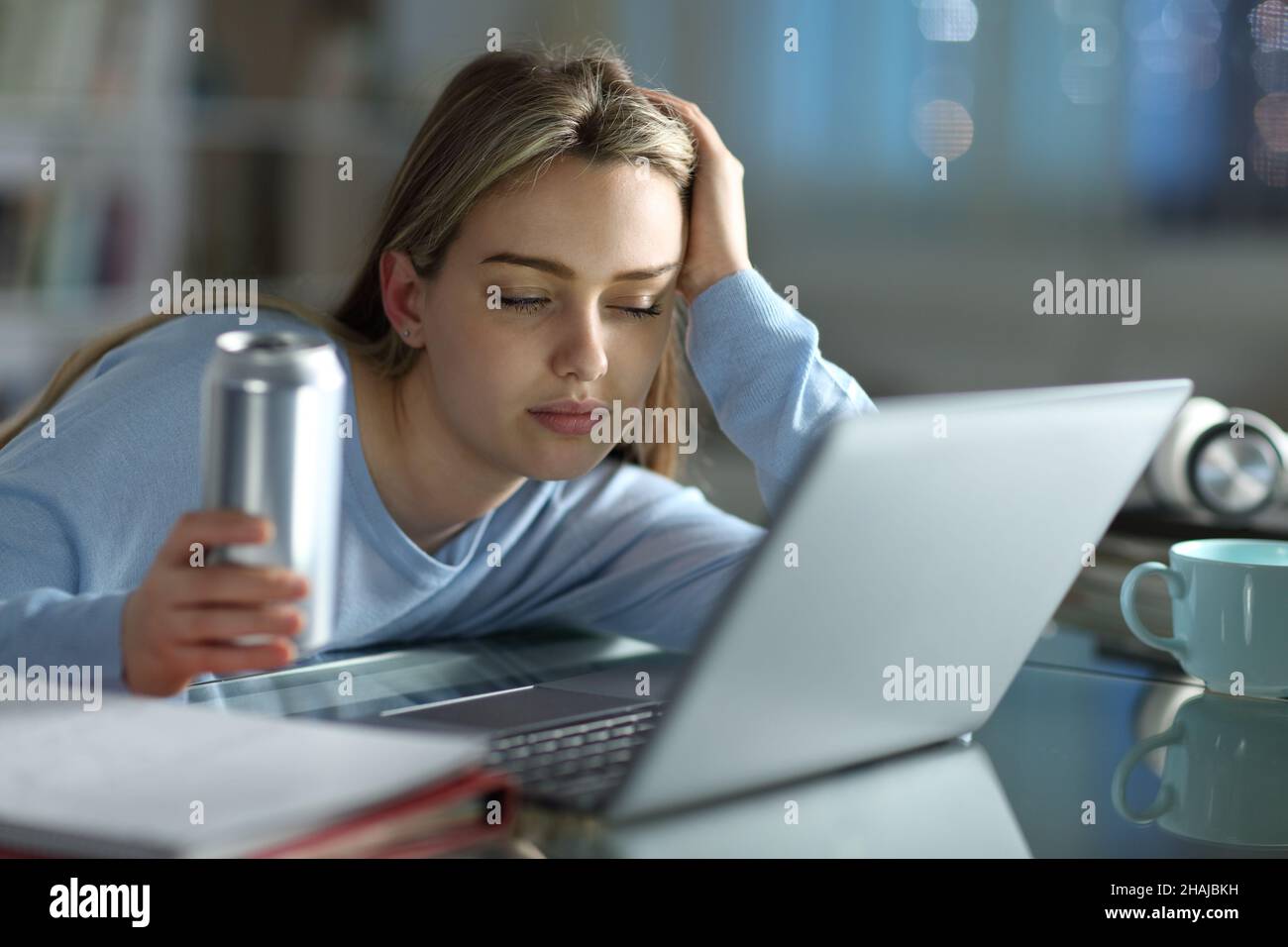 Étudiant endormi essayant d'étudier avec un ordinateur portable tenant une boisson énergétique dans la nuit à la maison Banque D'Images