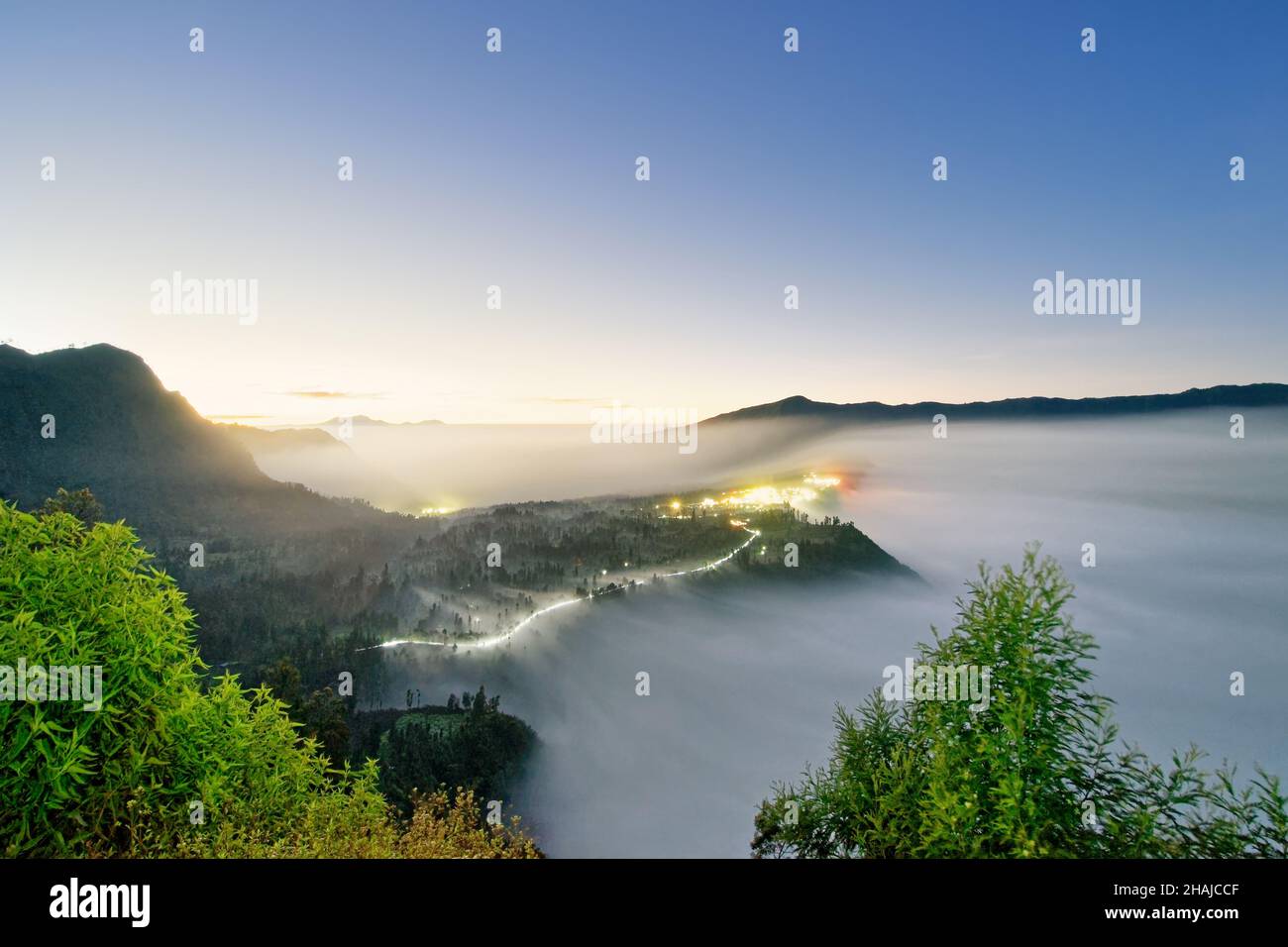 Brouillard au volcan Mt.Bromo au lever du soleil, le brouillard se déforme sur l'immense cratère, la piste lumineuse d'une route - emplacement : Indonésie, île de Java, Gunung Bromo, Natio Banque D'Images