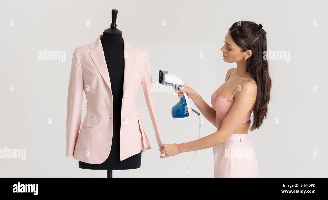 Angleterre, Royaume-Uni.2021. Jeune femme tenant une veste rose qui a été pressée.Maquette de tailleur noir. Banque D'Images