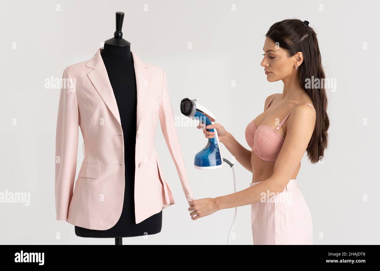 Angleterre, Royaume-Uni.2021. Jeune femme tenant une veste rose qui a été pressée.Maquette de tailleur noir. Banque D'Images