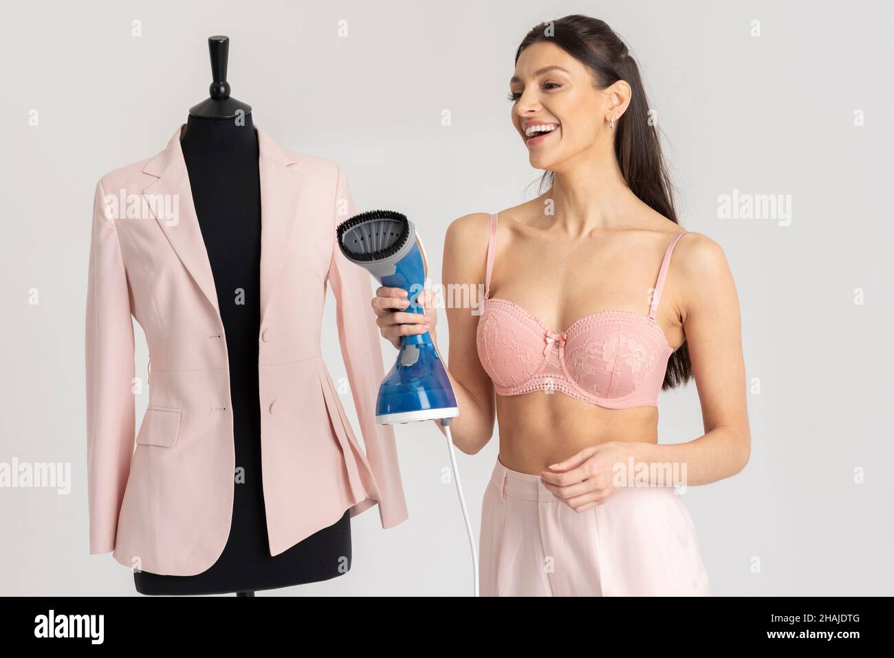 Angleterre, Royaume-Uni.2021. Jeune femme riant et tenant une veste rose qui a été pressée.Maquette de tailleur noir. Banque D'Images