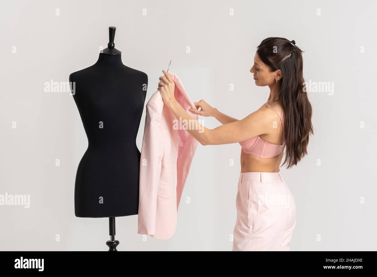 Angleterre, Royaume-Uni.2021. Jeune femme enlever une veste rose d'un mannequin de tailleurs après avoir appuyé. Banque D'Images