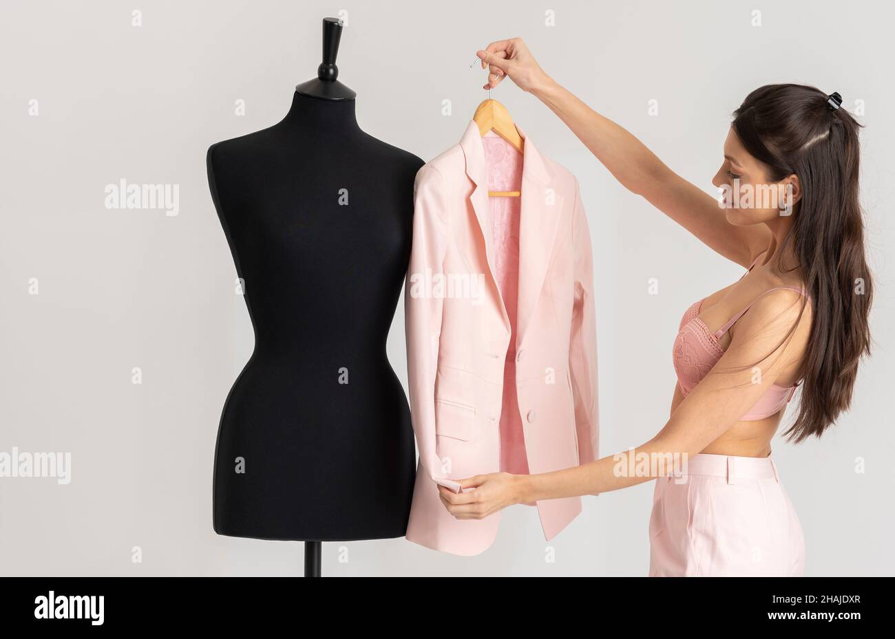 Angleterre, Royaume-Uni.2021. Jeune femme enlever une veste rose d'un mannequin de tailleurs après avoir appuyé. Banque D'Images
