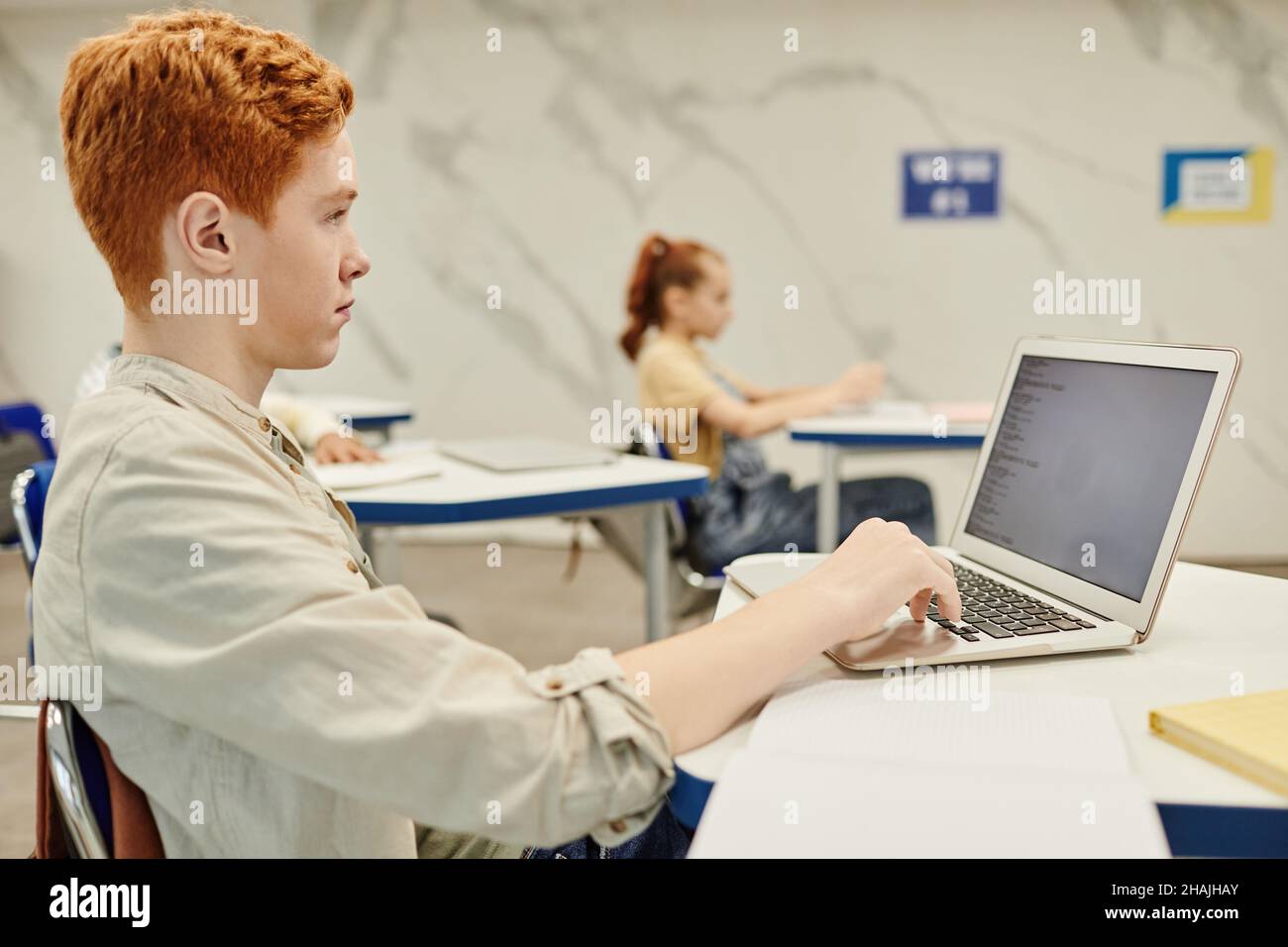 Portrait de l'adolescent aux cheveux rouges à l'aide d'un ordinateur portable tout en encodant dans la salle de classe, espace de copie Banque D'Images