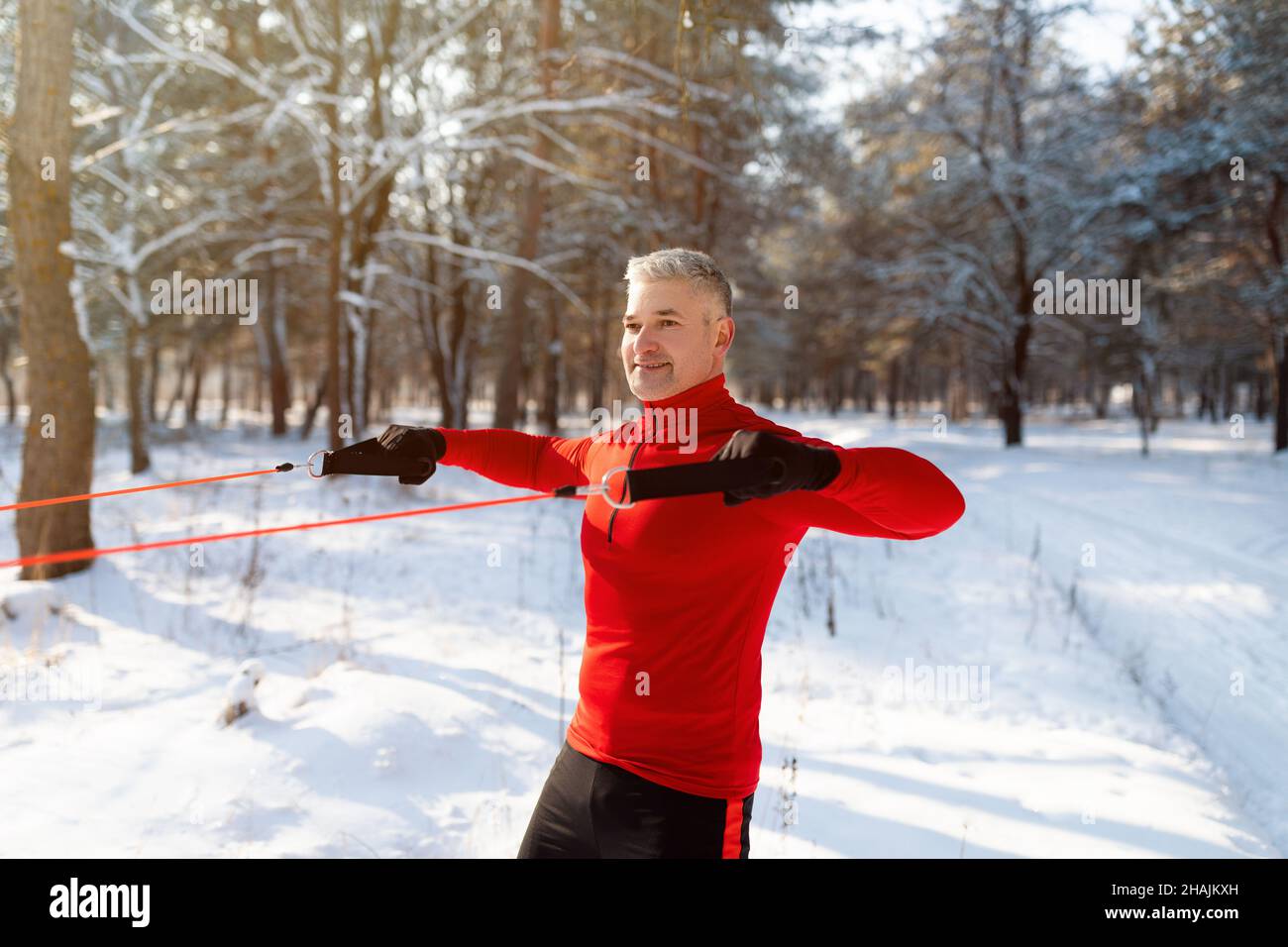 Entraînement fonctionnel.Sportif solide et mature s'entraînant avec des sangles de résistance au poids du corps au parc par temps de neige froid Banque D'Images