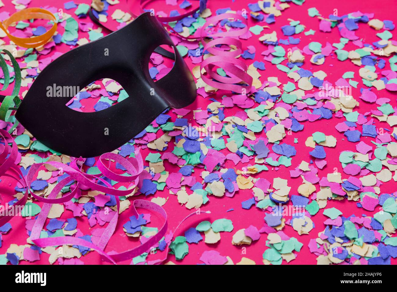 Carnaval confetti fond festif.Masque noir et cercles de papier colorés et lumineux sur rose.Modèle d'invitation à une fête Banque D'Images