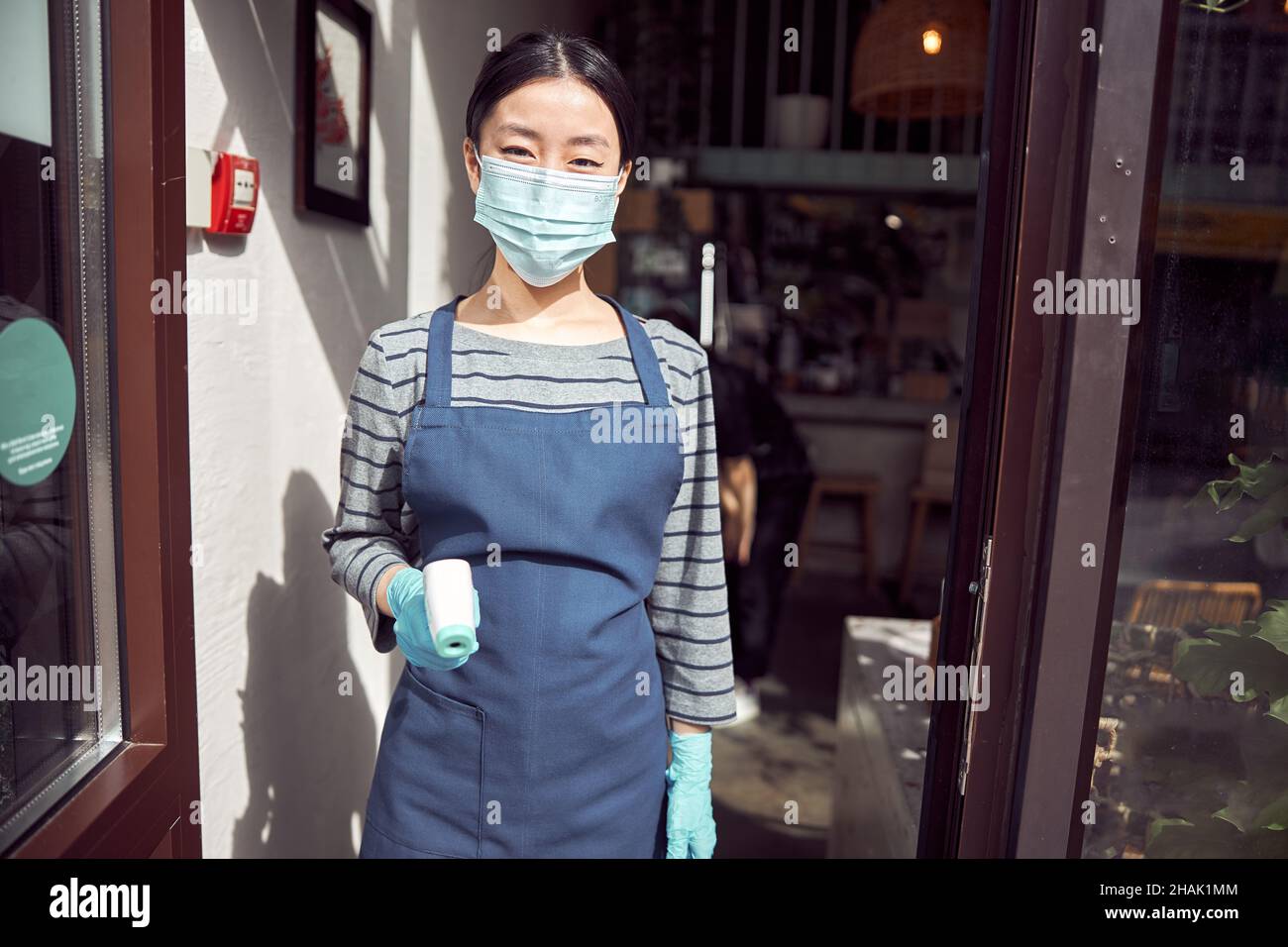 Femme asiatique utilisant un thermomètre laser pour vérifier la température avant le café Banque D'Images