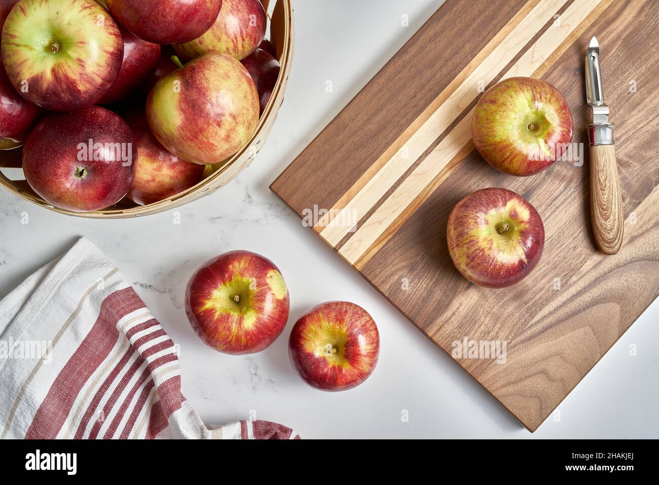 Pommes Cortland sur une planche à découper avec un éplucheur et plus de pommes dans un panier Banque D'Images
