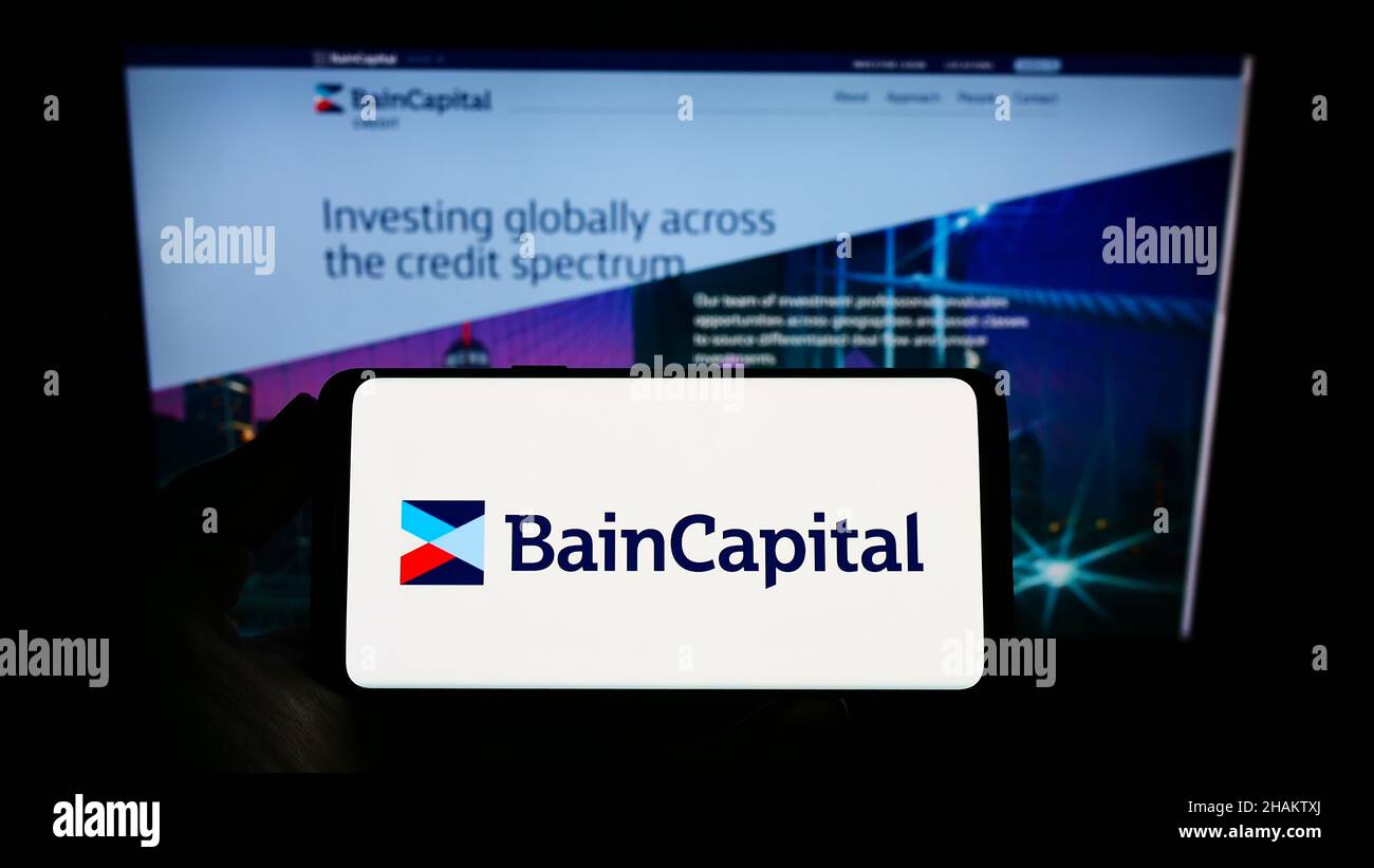 Personne tenant un téléphone portable avec le logo de la société d'investissement américaine bain Capital L.P. sur l'écran en face de la page Web.Mise au point sur l'affichage du téléphone. Banque D'Images