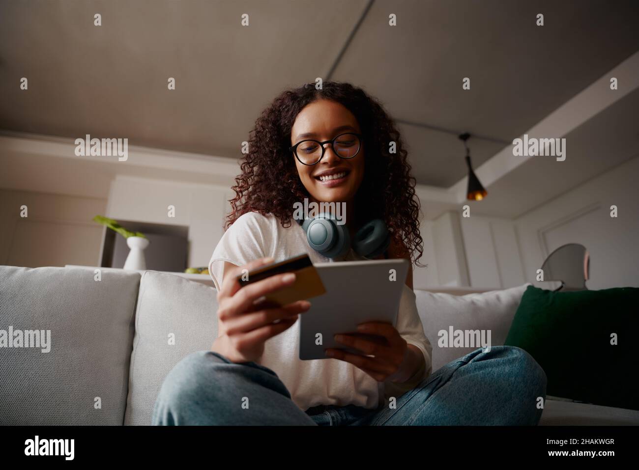 Happy Multi-cultural femme faisant l'achat en ligne sur tablette tout en étant sur le canapé, basse angle Banque D'Images