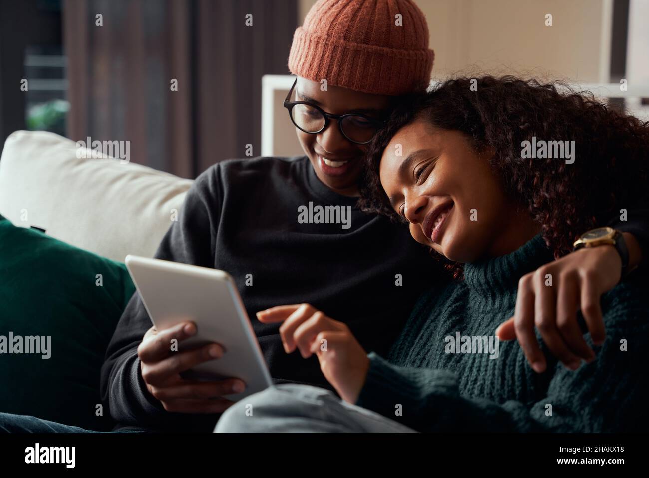 Mignon couple adulte, multi-ethnique, souriant à la tablette sur le canapé dans l'appartement moderne Banque D'Images