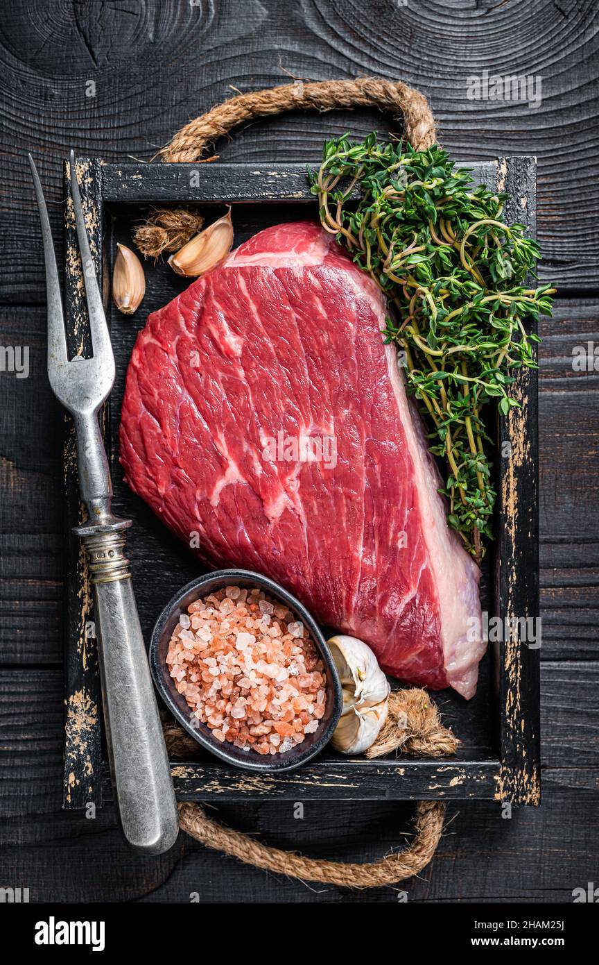 Steak de viande de bœuf coupé au sommet de la sirloine crue ou Picanha dans un plateau en bois avec des herbes. Arrière-plan en bois noir. Vue de dessus Banque D'Images