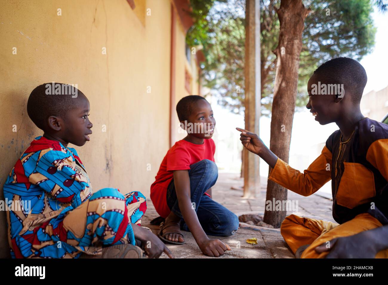 Trois garçons africains s'assoient sur le sol, plaisantent dans la cour à l'extérieur pour jouer à des jeux amusants Banque D'Images