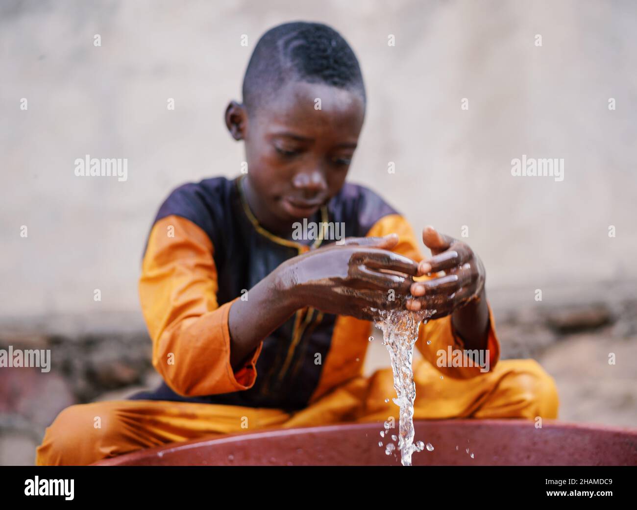 Gros plan portrait d'un jeune garçon africain Profitez et jouez avec de l'eau propre fraîche du seau à l'extérieur Banque D'Images