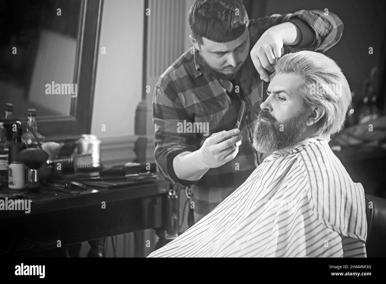 Coiffeur professionnel coupant les cheveux d'homme brutal dans le salon de beauté. Banque D'Images