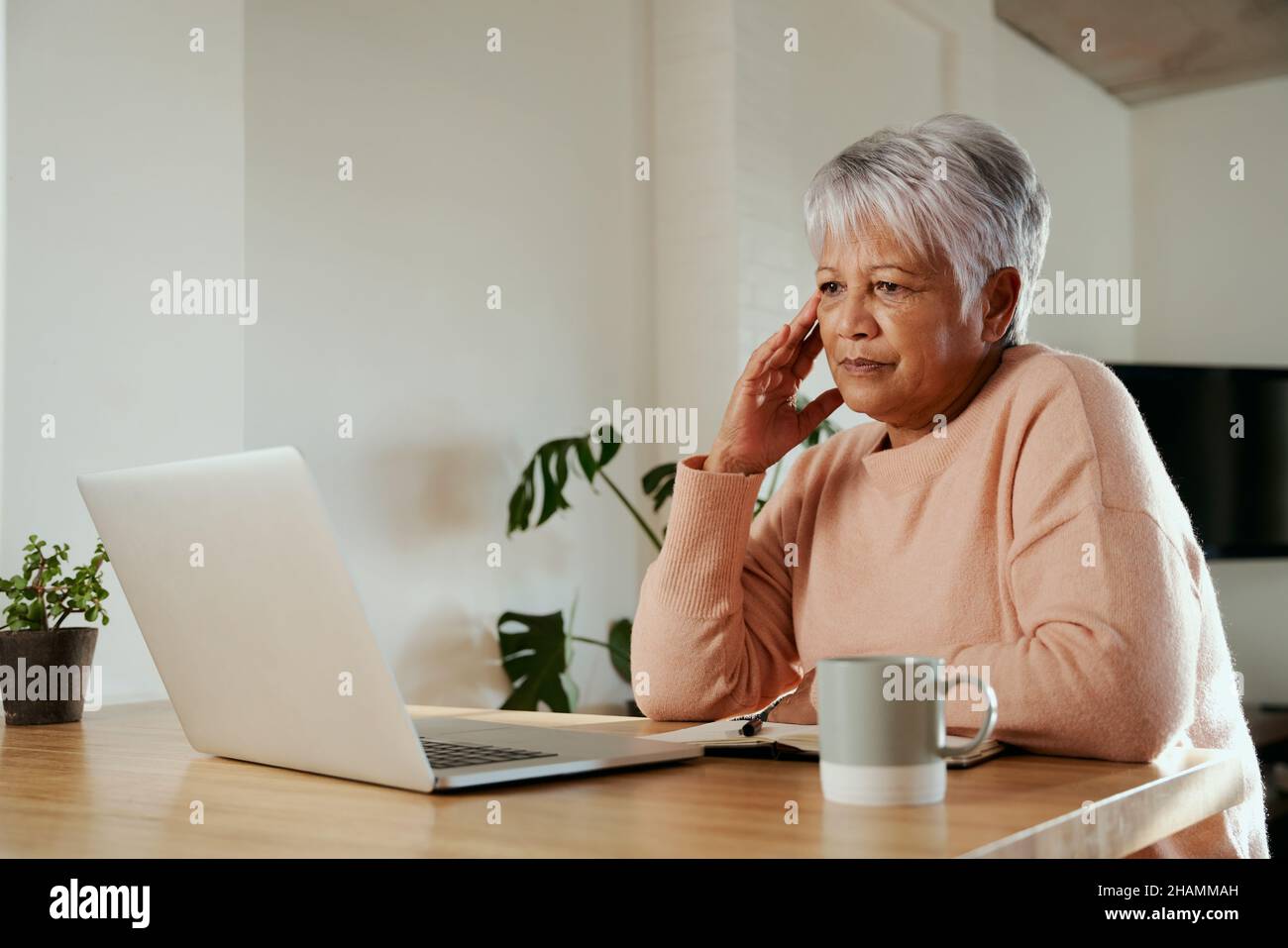 Une femme âgée de plusieurs ethnies s'inquiétait des finances lorsqu'elle regarchait un ordinateur portable.Asseyez-vous avec mal de tête au comptoir de cuisine moderne à la maison. Banque D'Images