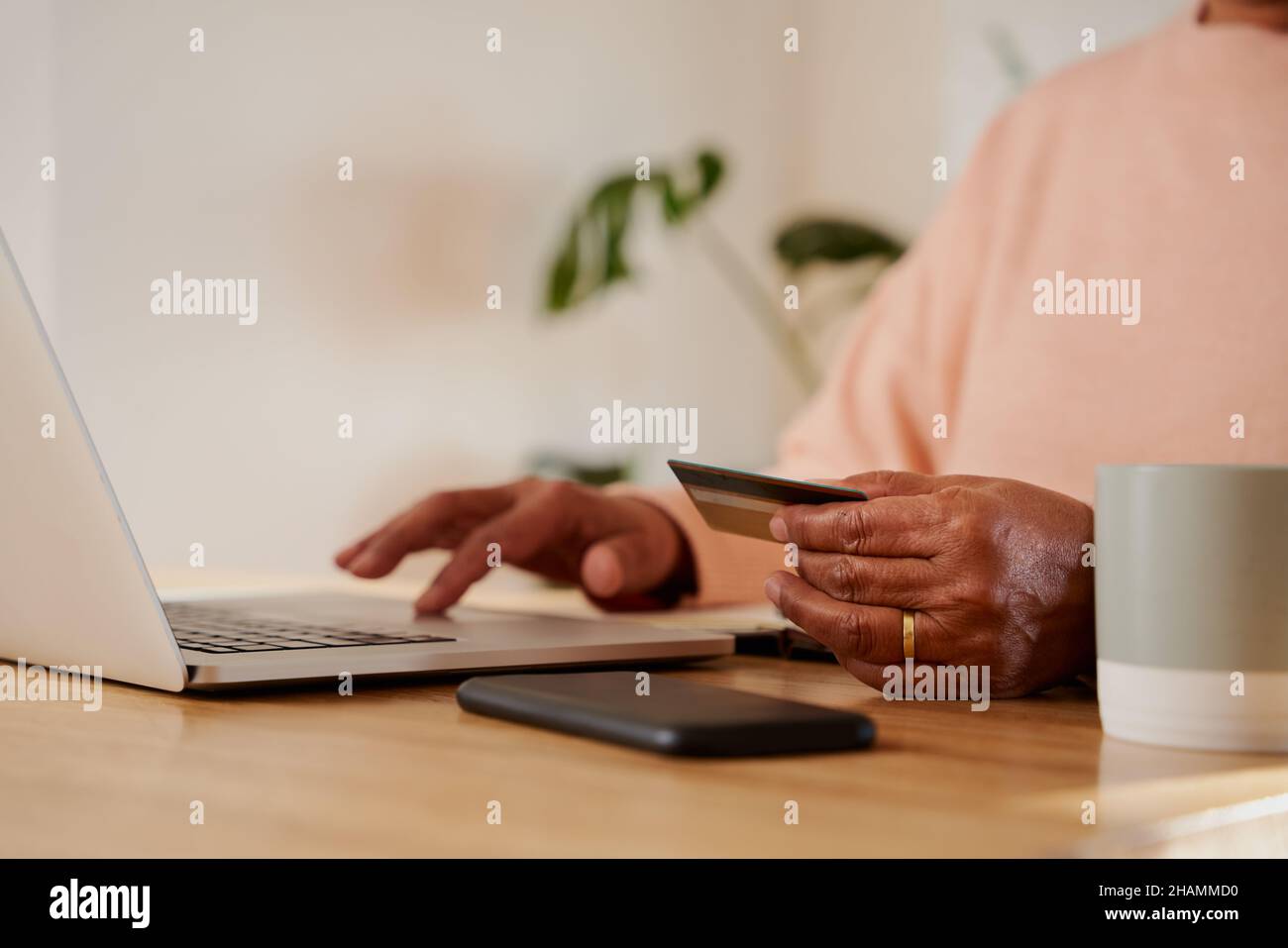 Mains de femmes âgées multiethniques effectuant le paiement en ligne sur ordinateur portable, assis au comptoir de cuisine. Banque D'Images