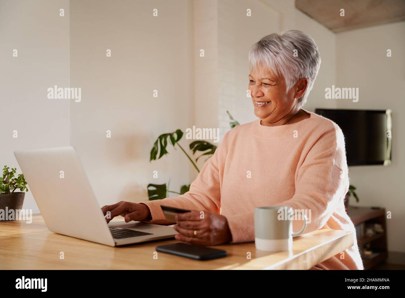 Femme âgée, multi-ethnique, souriant pendant un appel en ligne.Salon avec ordinateur portable au comptoir de la cuisine. Banque D'Images
