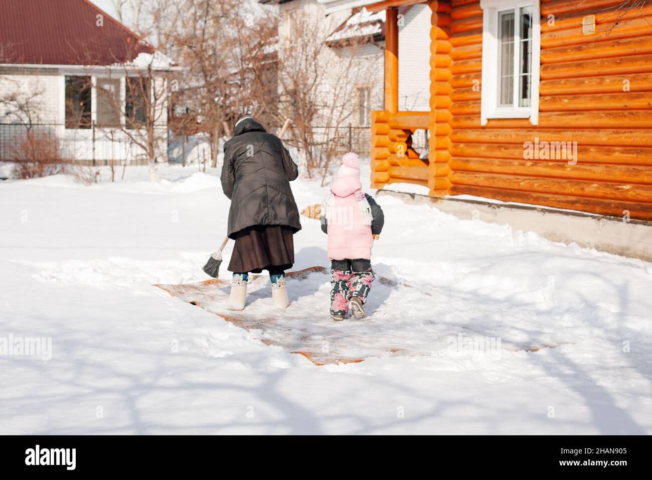 La femme enseigne à l'enfant à nettoyer la moquette.La famille est engagée dans le nettoyage écologique de tapis par méthode traditionnelle avec l'aide de la neige fraîche et le balai à proximité Banque D'Images