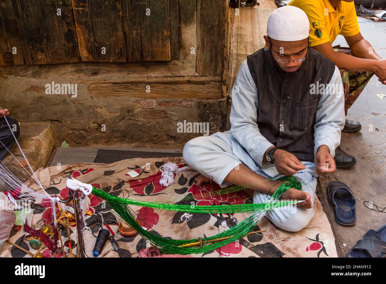 Un musulman népalais tient la corde par ses orteils comme il fait un collier de perles dans le bazar de Potey à Katmandou, Népal. Banque D'Images