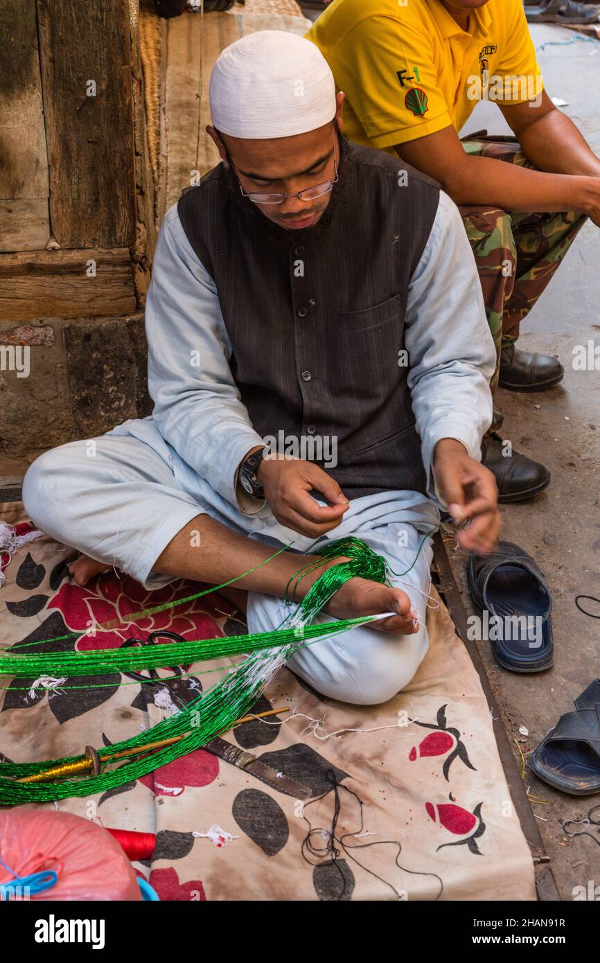 Un musulman népalais tient la corde par ses orteils comme il fait un collier de perles dans le bazar de Potey à Katmandou, Népal. Banque D'Images